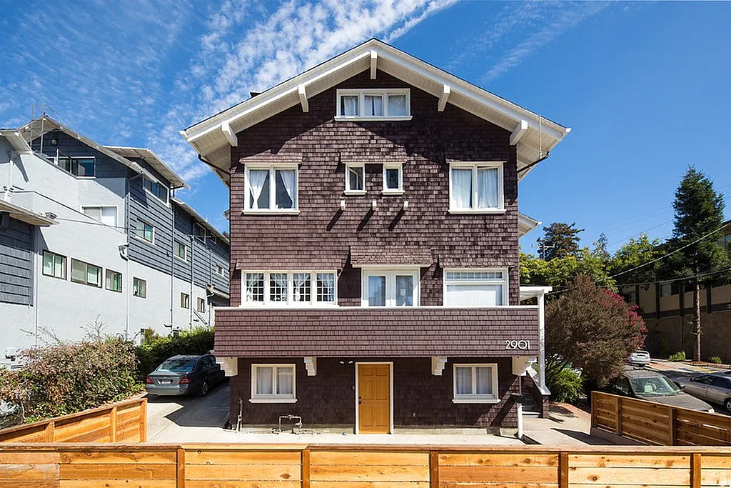Charming multi-story home with classic architecture, featuring a wooden fence, manicured foliage, and picturesque neighborhood setting under a clear blue sky.