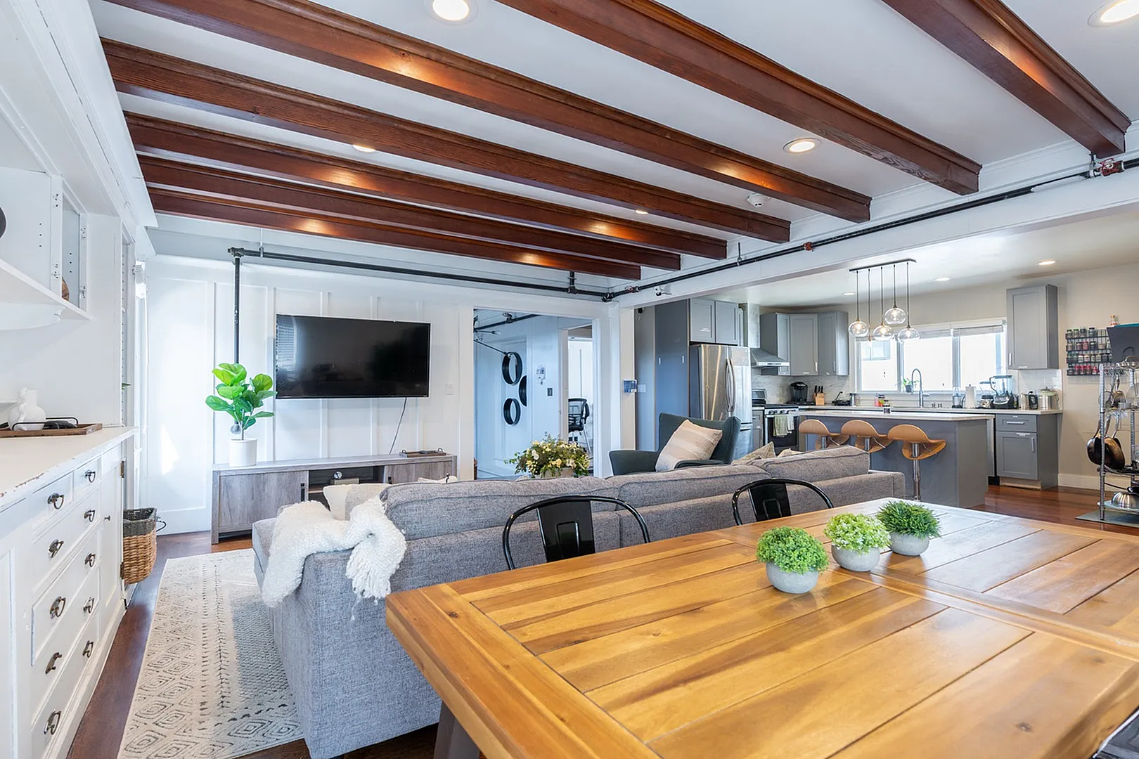Luxurious open-concept living room and kitchen featuring modern decor, exposed wooden beams, and abundant natural light.