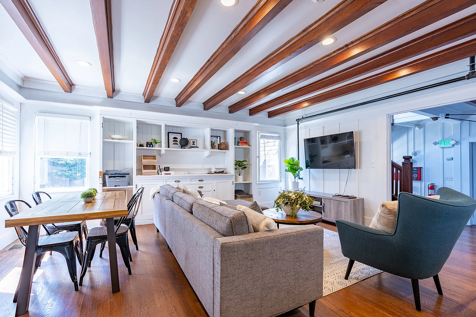 Bright and elegant living room with exposed wooden beams, cozy seating, and a stylish dining area, offering a perfect blend of modern design and comfort.