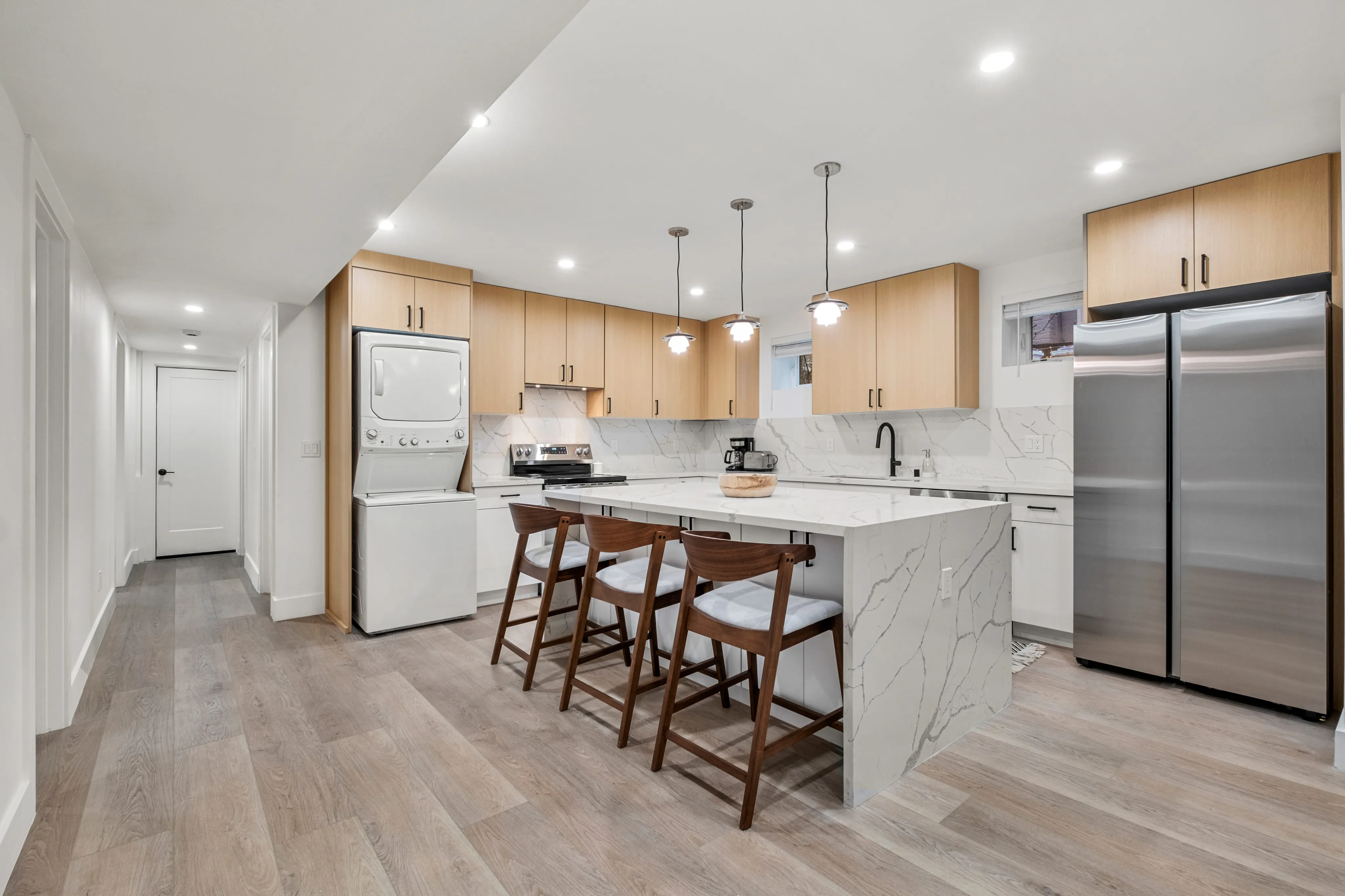 Modern kitchen with elegant marble countertops, sleek stainless steel appliances, and chic pendant lighting, complemented by stylish wooden cabinetry and seating.