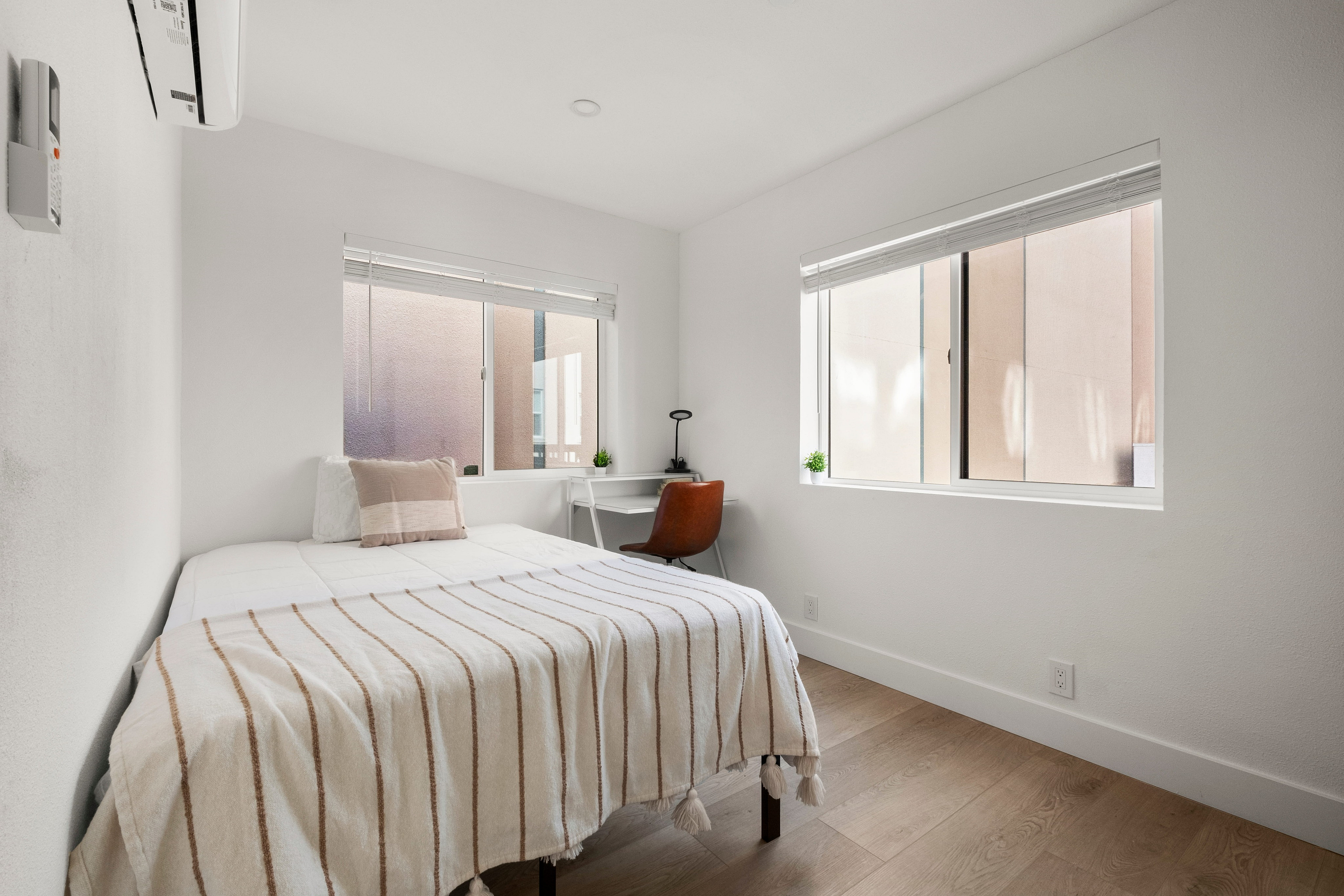Bright and cozy bedroom featuring a comfortable bed with striped linens, large windows, and sleek wooden flooring.