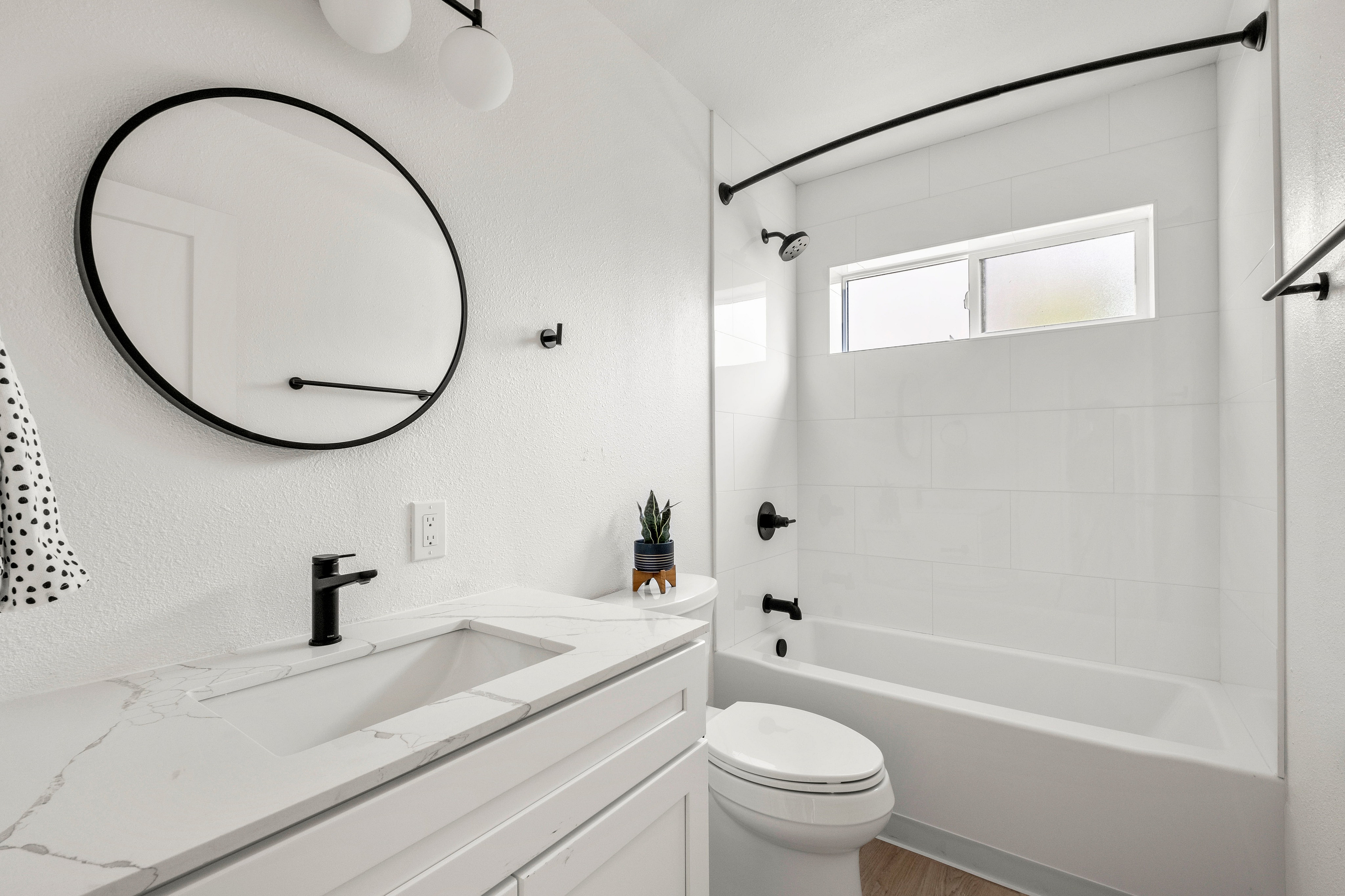 Sleek modern bathroom with elegant marble countertop, stylish black fixtures, and a minimalist round mirror.