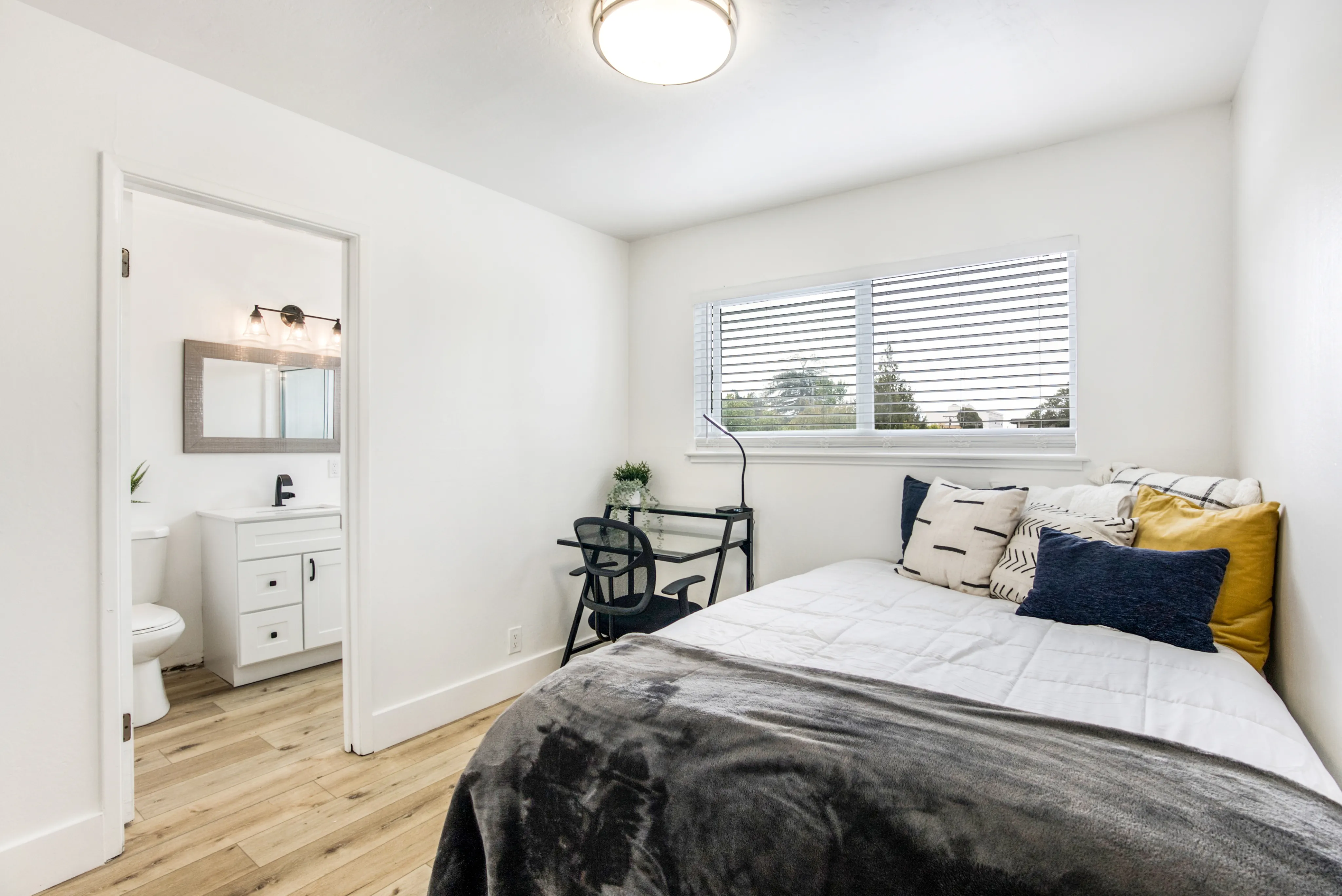 Bright and cozy bedroom featuring modern decor, large window with blinds, and a private en-suite bathroom.