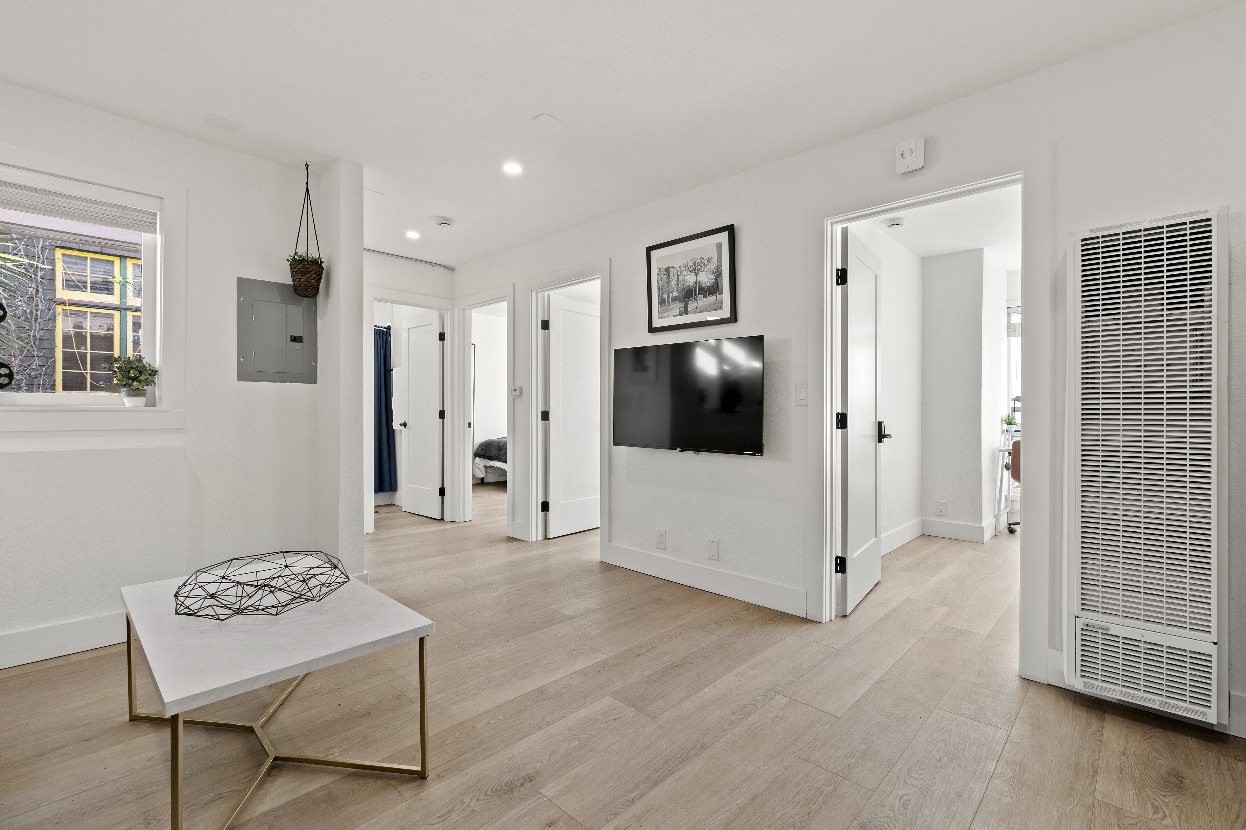 Bright and modern apartment interior with sleek hardwood floors, wall-mounted TV, and contemporary decor.