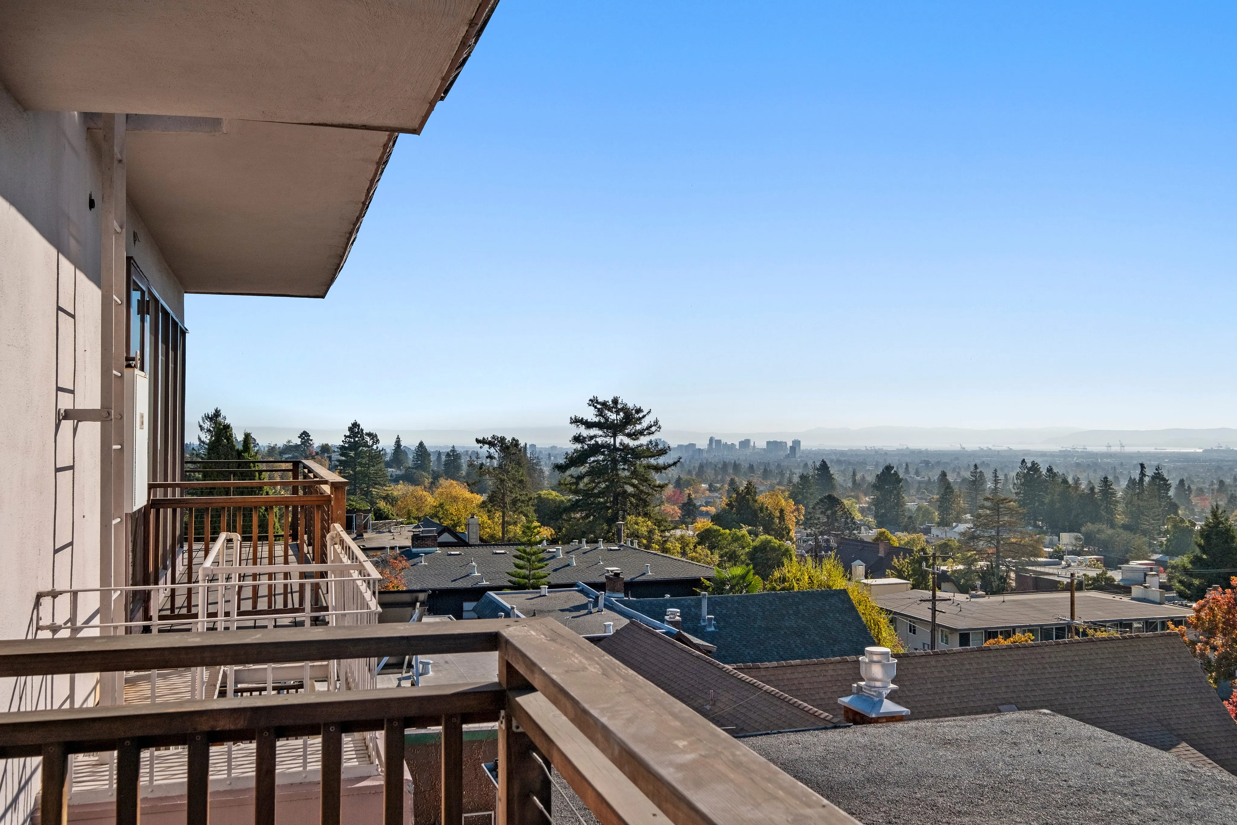 Stunning balcony view showcasing a panoramic cityscape against a clear blue sky, with lush greenery and distant skyline.