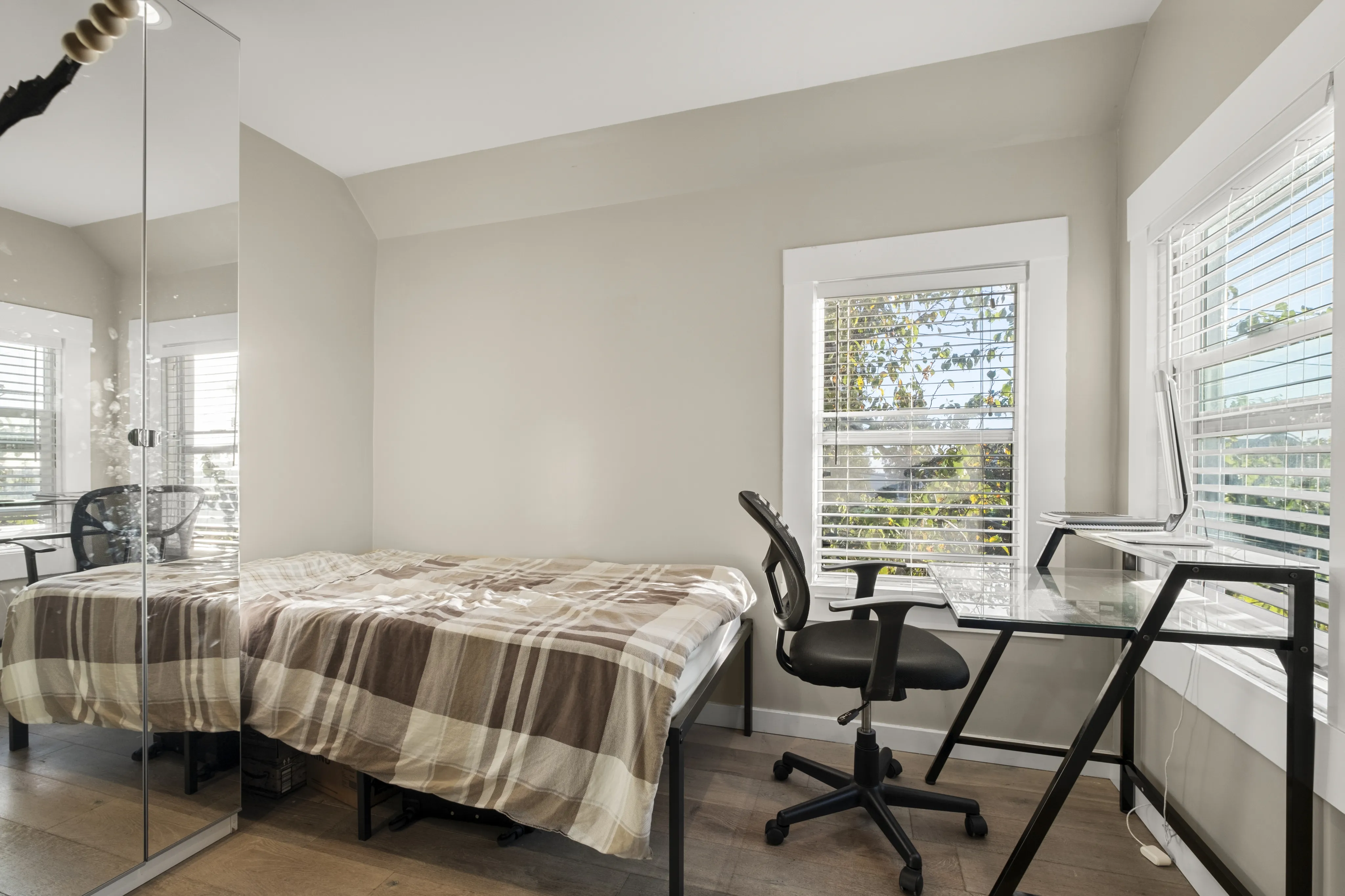 Bright, cozy bedroom with a stylish glass desk and comfy office chair, featuring modern decor and a sun-drenched window view.