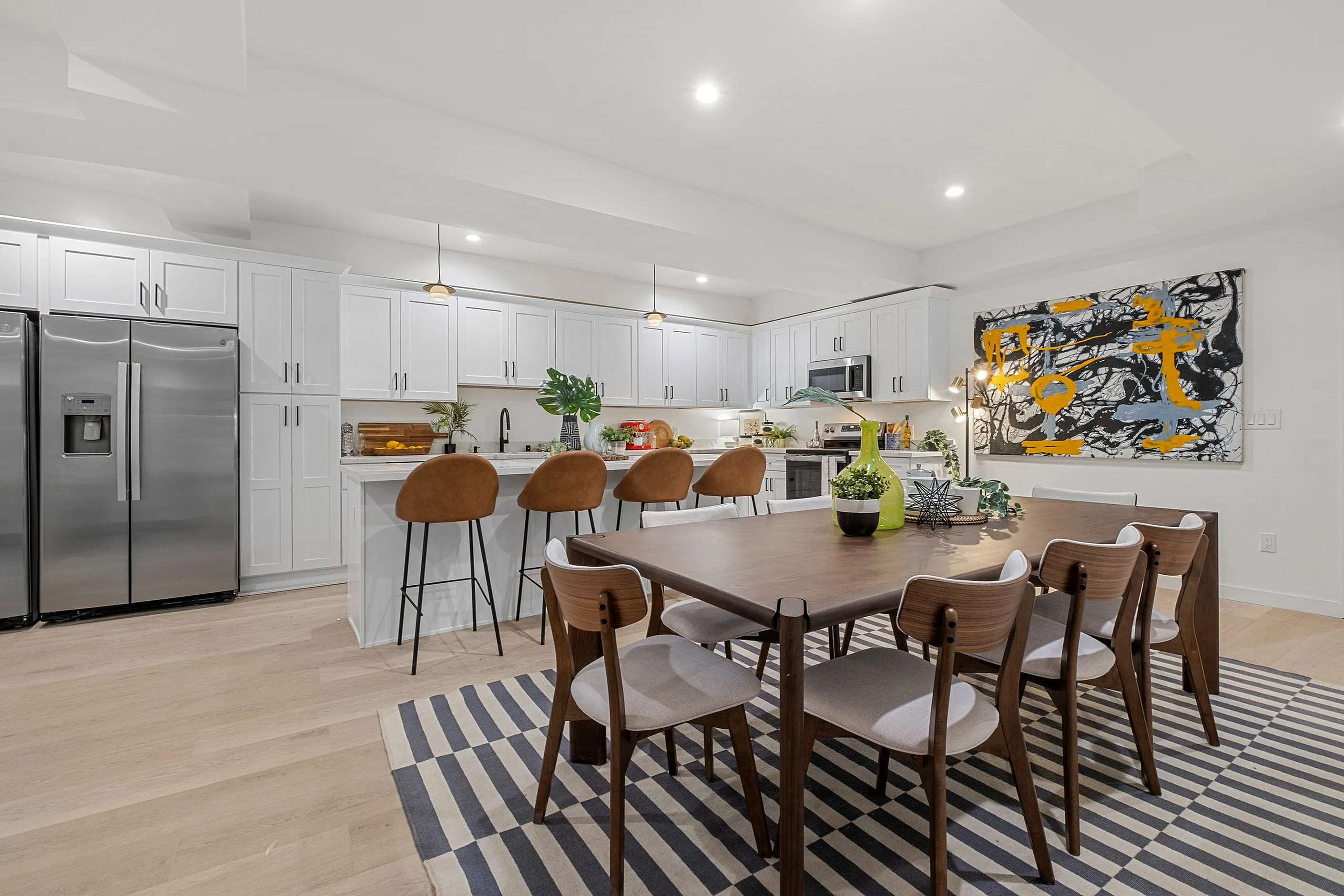 Modern open-concept kitchen and dining area featuring sleek white cabinets, spacious island with stylish barstools, and contemporary artwork.