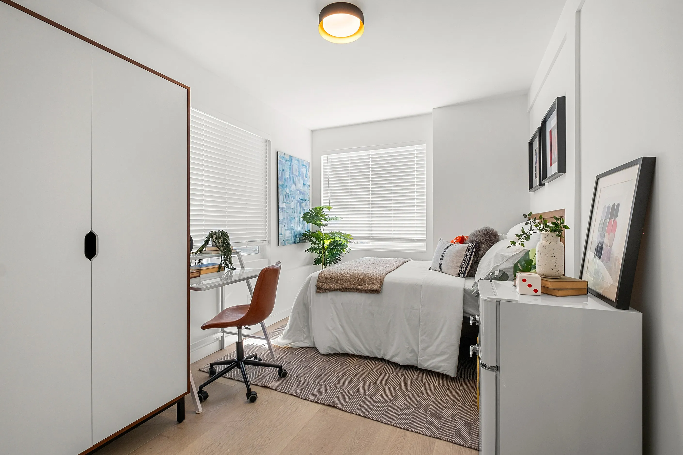 Bright and airy bedroom with modern decor, featuring a cozy bed, sleek desk area, and natural light streaming through large windows.