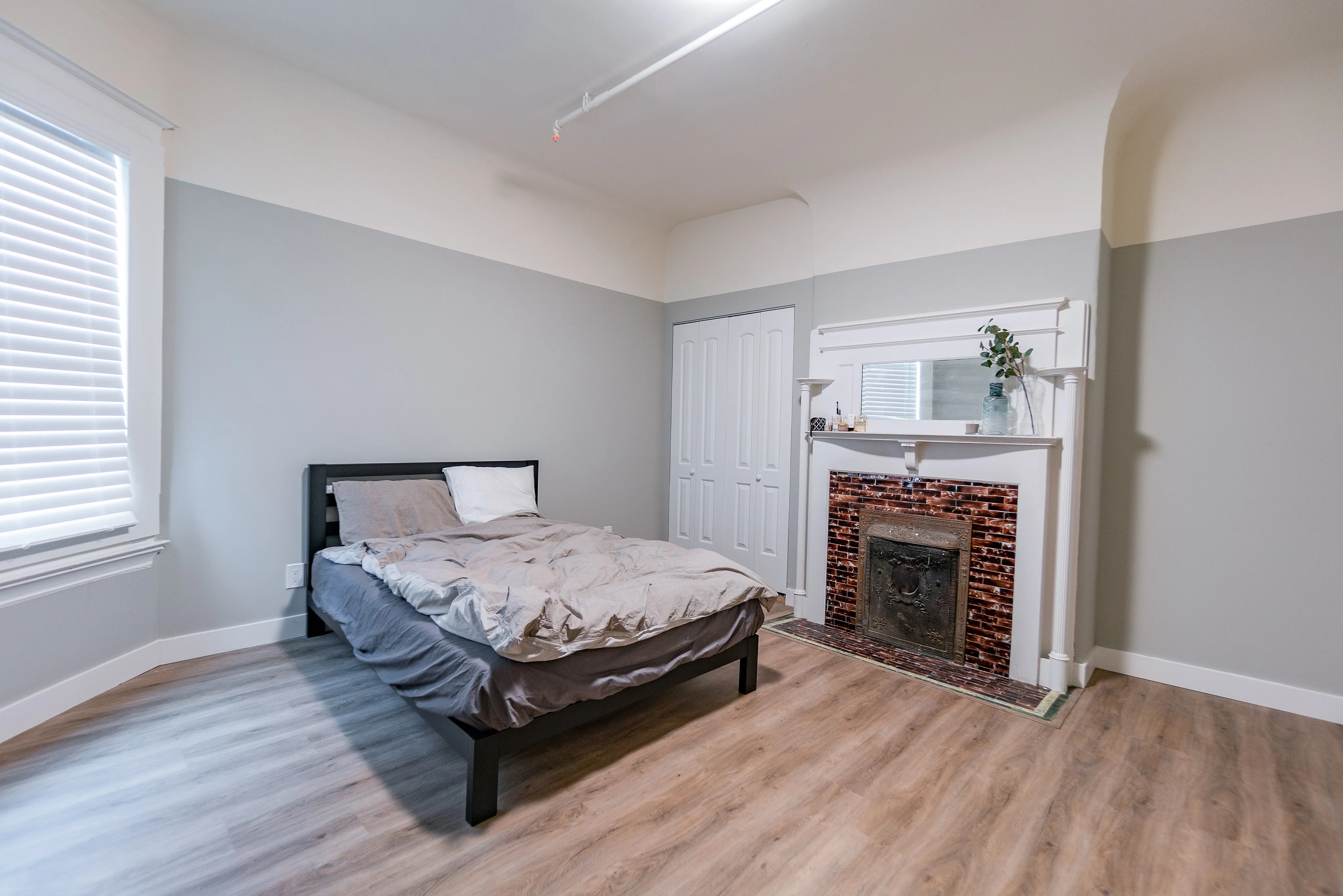 Charming bedroom with a cozy bed, elegant fireplace, and abundant natural light from large window, showcasing stylish hardwood floors.