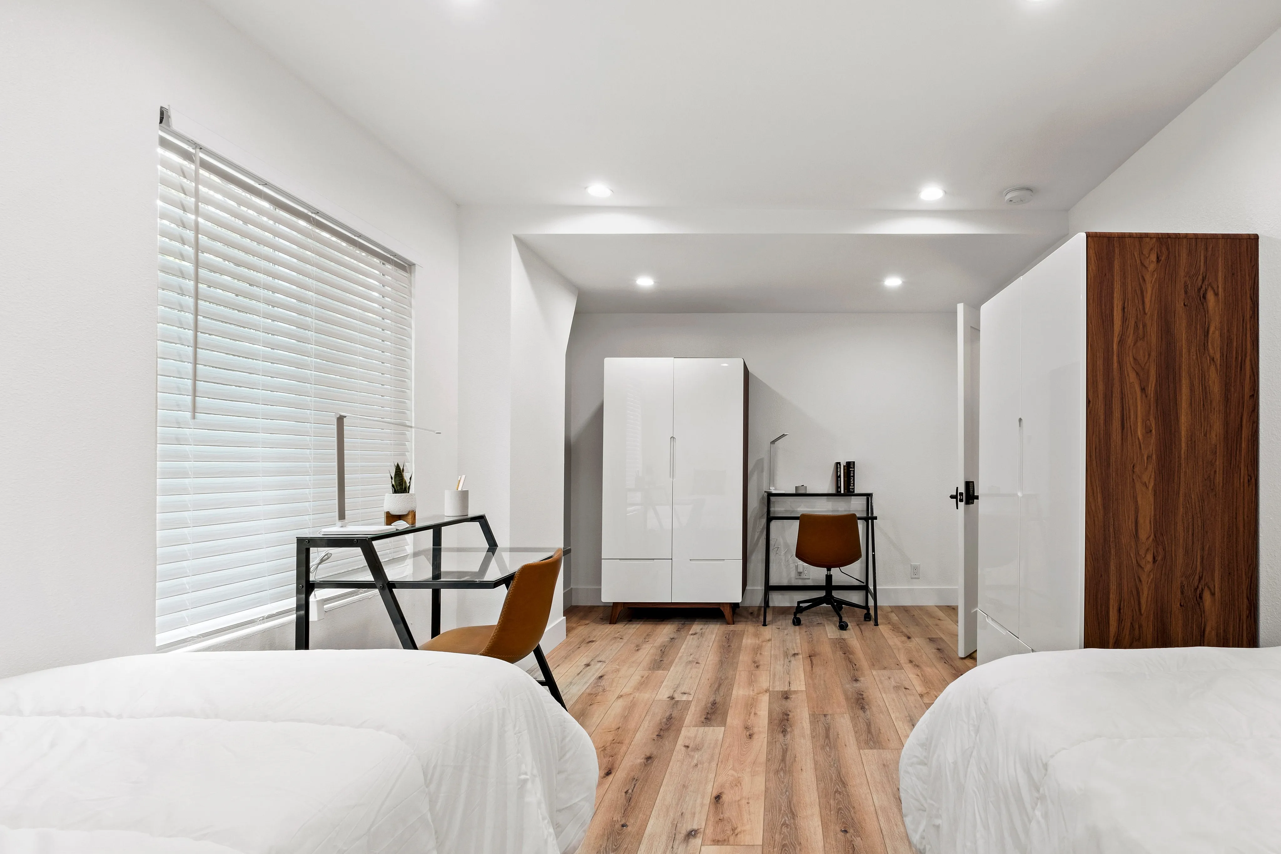 Bright and stylish bedroom with modern furniture, featuring two beds, a sleek work desk, and ample natural light for a cozy living experience.