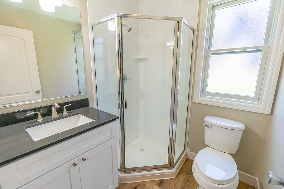 Bright and modern bathroom with sleek glass shower, elegant vanity, and natural light from a frosted window.