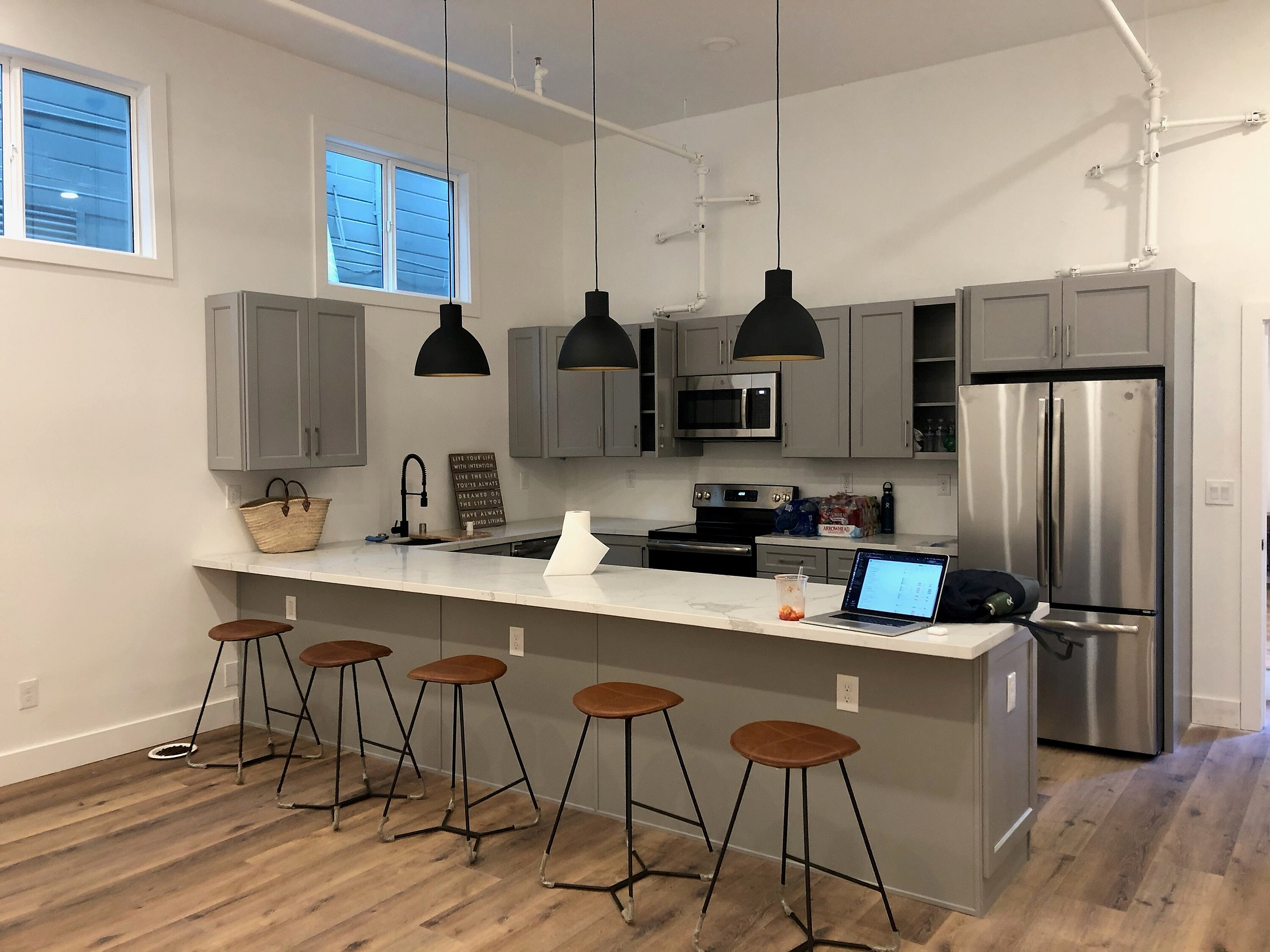 Modern kitchen space with sleek gray cabinets, stainless steel appliances, and chic pendant lighting above a spacious breakfast bar with stylish stools.