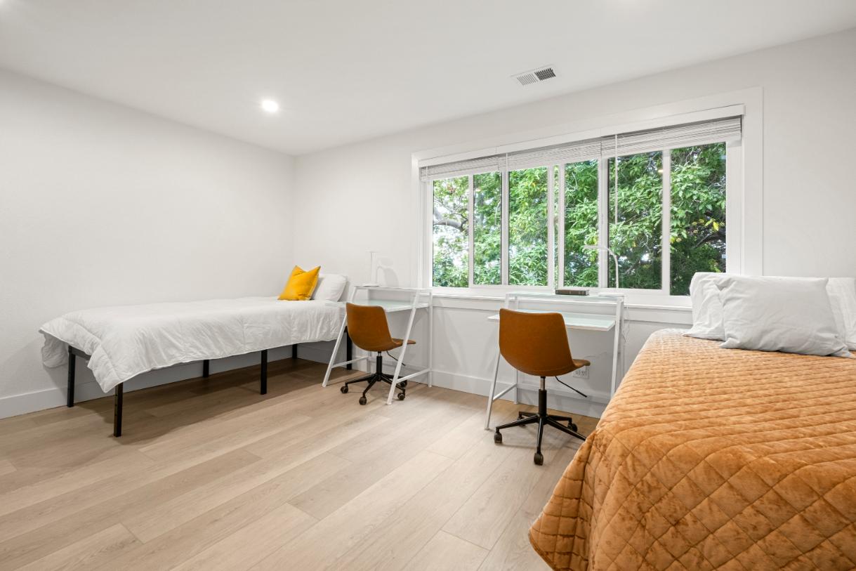 Modern bedroom interior showcasing minimalist design with sleek desks, cozy beds, and abundant natural lighting through large windows
