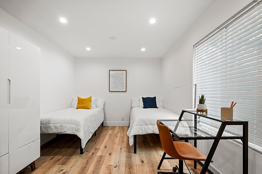 Bright and modern bedroom with twin beds, elegant wood flooring, and a stylish workspace by the window.