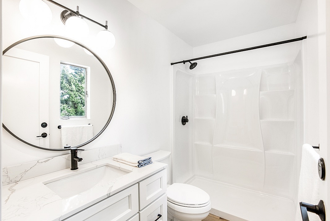 Bright and modern bathroom boasting a sleek marble vanity, circular mirror, and elegant shower.