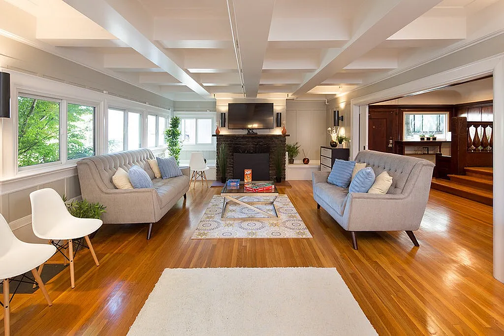 Elegant living room featuring cozy gray sofas, vibrant hardwood floors, large windows with green views, and a modern entertainment center with a fireplace.