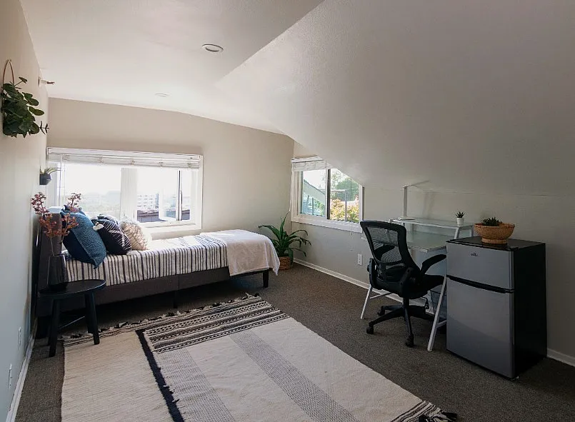 Bright and cozy attic bedroom with modern decor, featuring a comfortable bed, stylish desk area, and large windows offering scenic city views.