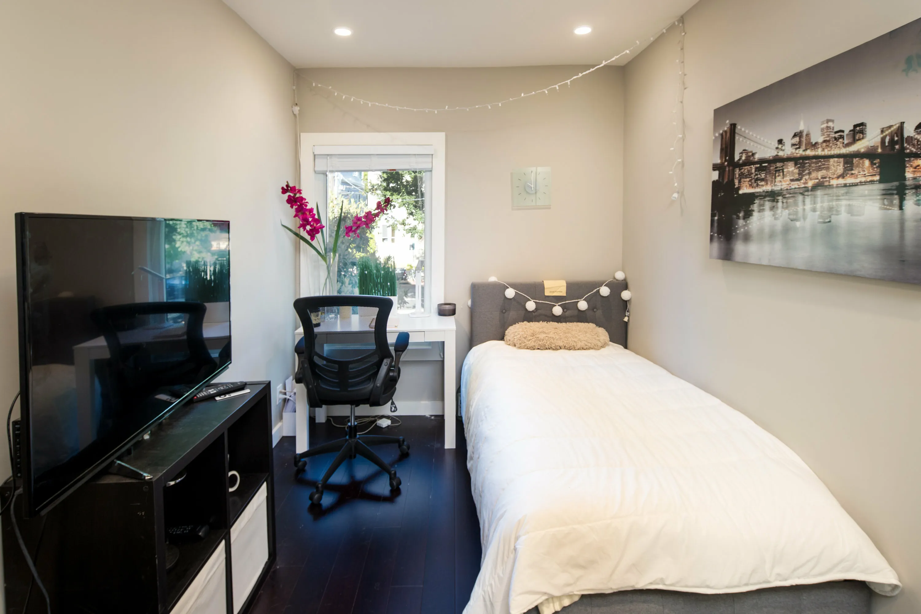 Cozy bedroom with stylish decor featuring a comfortable bed, modern desk, and vibrant artwork, illuminated by soft natural light.
