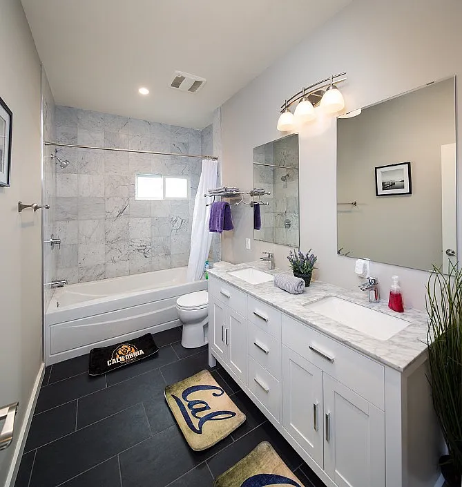 Elegant bathroom featuring double vanity with marble countertops, sleek tile flooring, and shower-tub combo accented by stylish decor.
