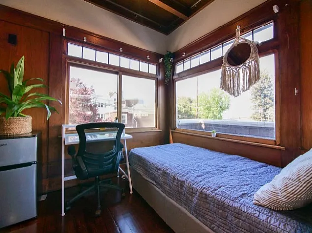Charming bedroom with large windows offering natural light, a cozy bed, and a workspace with a serene view.