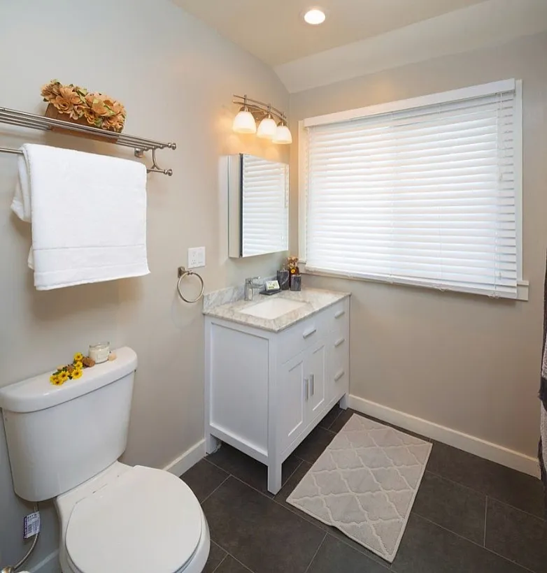 Elegant bathroom design featuring a modern vanity with marble countertop, large window with blinds, and sleek tile flooring for a luxurious touch.