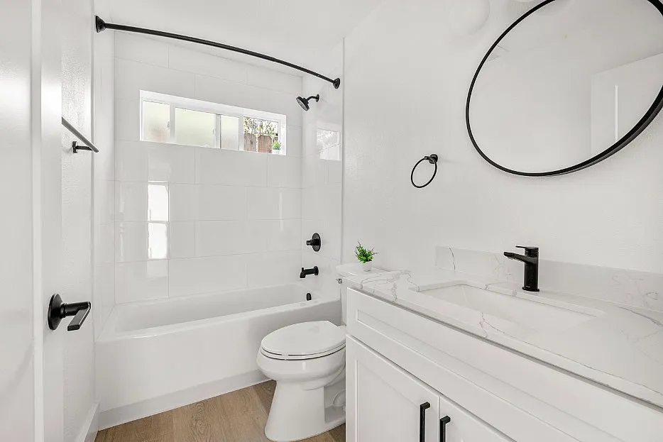 Elegant bathroom with a sleek white design, featuring a modern vanity, round mirror, and a spacious bathtub.