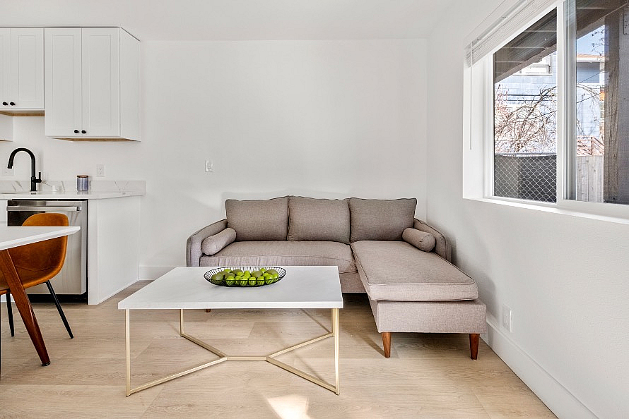Bright and modern apartment living area featuring a cozy sectional sofa, and sleek white cabinets.