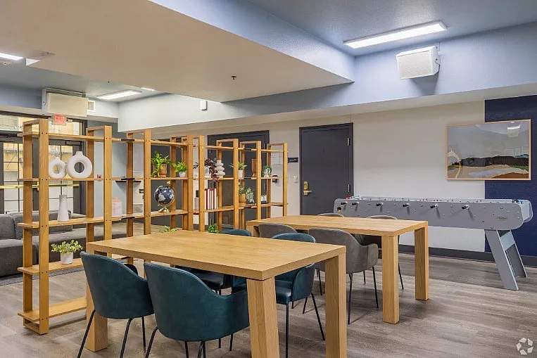 Modern communal space with stylish wooden furniture, vibrant green chairs, and a foosball table, perfect for relaxation and socializing.