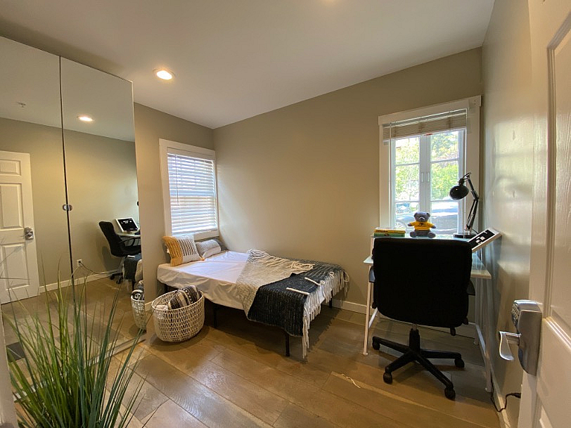 Cozy bedroom with modern decor, featuring a comfortable bed, stylish desk with chair, and ample natural light from large window.