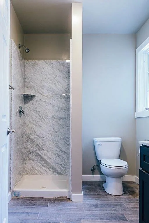 Elegant bathroom featuring a modern marble shower and sleek porcelain toilet, full of natural light.