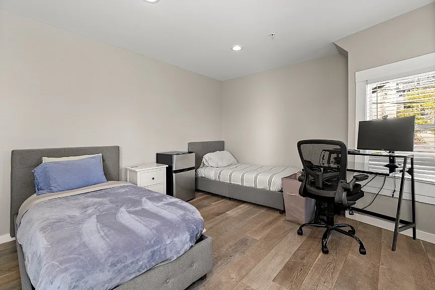 Bright and versatile bedroom featuring two cozy beds, modern decor, and a sleek workspace with a computer desk by the window.