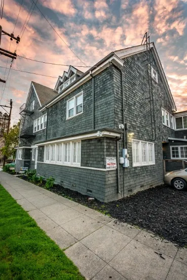 Charming multi-story home with vintage architecture, featuring rustic gray siding and nestled in a picturesque neighborhood under a vibrant sunset sky.