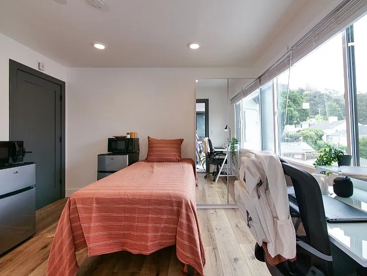 Bright modern bedroom with wood flooring, sleek workspace, and large windows offering scenic views.