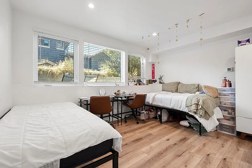 Bright and inviting bedroom with two cozy beds, stylish hardwood floors, and modern decor, enhanced by large windows offering natural light and garden views.