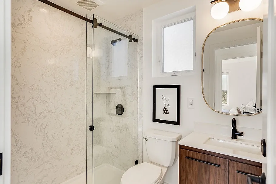 Sleek modern bathroom featuring marble walls, glass shower door, elegant mirror, and stylish fixtures.