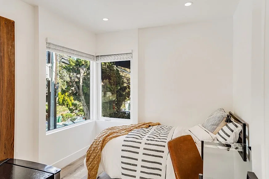 Cozy bedroom with a stylish bed and large windows offering a scenic outdoor view, flooding the space with natural light.
