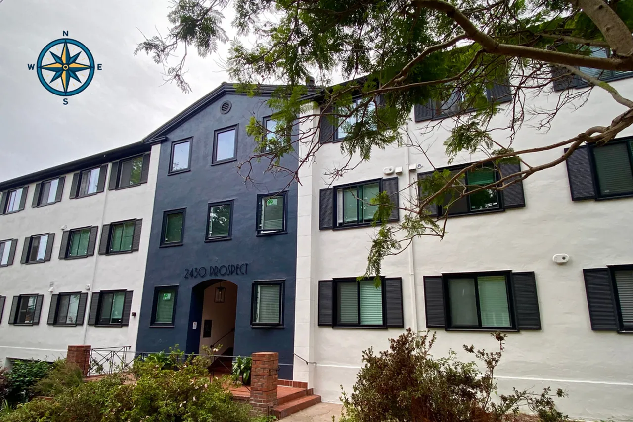 Charming three-story building with modern black and white exterior, surrounded by lush greenery, perfect for a cozy, community-focused lifestyle.