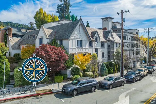 Elegant Tudor-style apartment building with charming gabled roofs, surrounded by vibrant autumn foliage and situated on a scenic, tree-lined street.