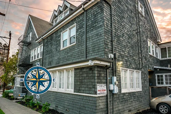 Charming grey shingle-style apartment building with classic windows, nestled on a scenic street corner at dusk.