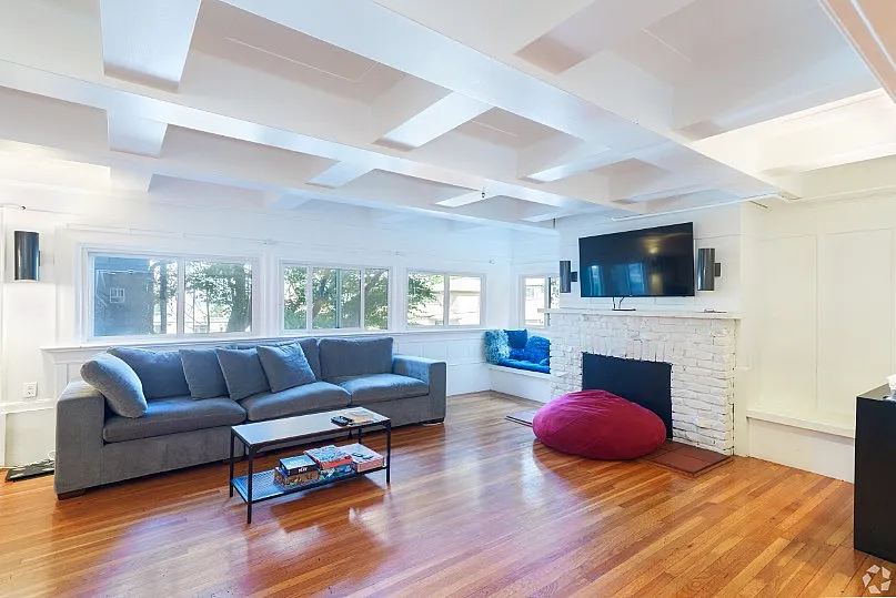 Bright and inviting living room with modern decor, featuring a cozy gray sofa, white brick fireplace, and large windows offering abundant natural light.