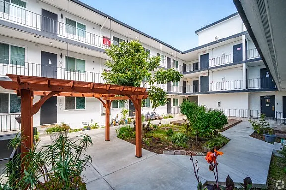 Charming apartment courtyard with lush greenery and a wooden pergola, showcasing a peaceful community atmosphere.