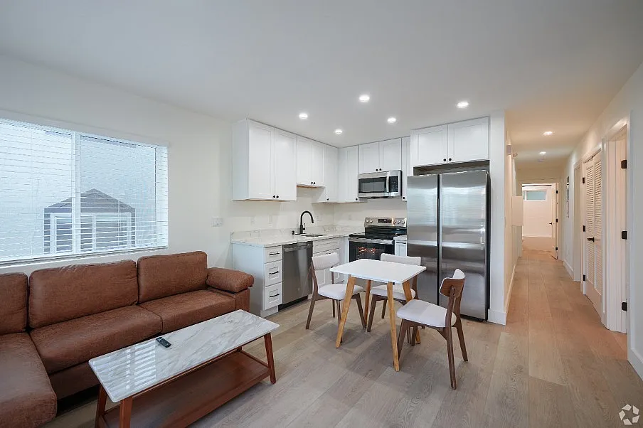 Modern open-concept living space featuring a sleek kitchen, cozy brown sofa, and chic dining area with natural light.