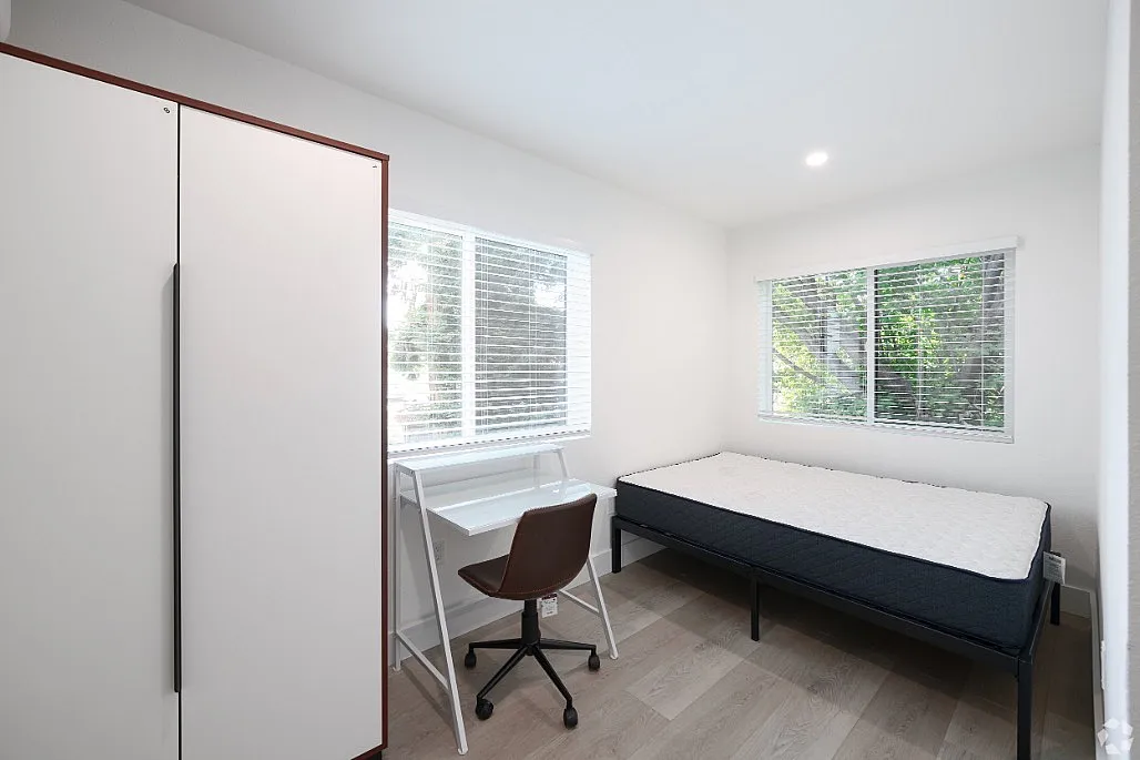 Bright and cozy bedroom with large windows, featuring a comfortable bed, sleek wardrobe, and modern study area.