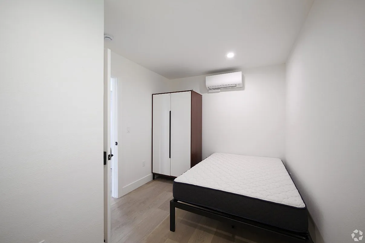 Bright and modern bedroom featuring sleek furnishings, airy white walls, and a minimalist wardrobe.