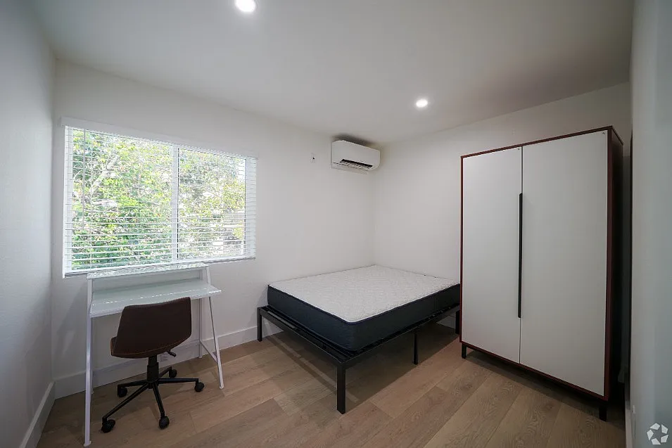 Bright and cozy bedroom featuring a spacious wardrobe, elegant desk, and large window with scenic greenery views.