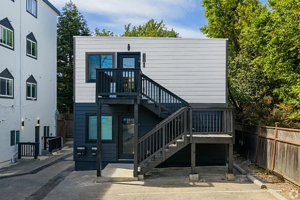 Charming modern duplex with a sleek exterior, highlighted by a stylish staircase and surrounded by lush greenery.
