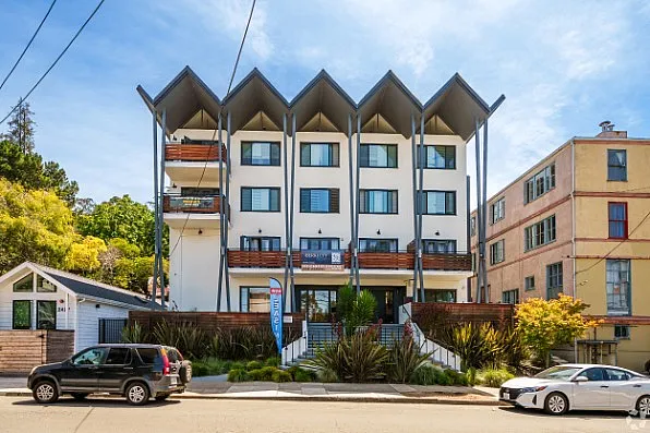 Modern apartment building with unique architectural design, featuring large windows, balconies, and lush landscaping in a vibrant neighborhood.