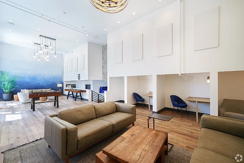 Modern apartment lounge featuring cozy seating, stylish wooden flooring, foosball table, and inviting workspace alcoves.