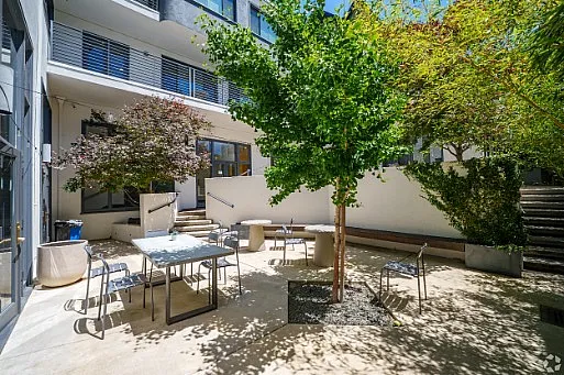 Chic outdoor patio with modern seating, lush greenery, and ample natural light in a serene apartment courtyard.