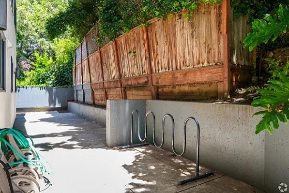 Charming outdoor patio with wooden fencing, lush greenery, and convenient bike racks.